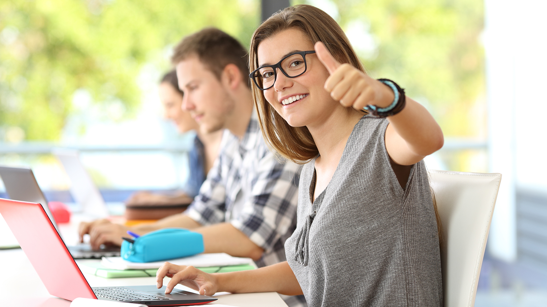 Glückliche Studentin mit Brille sitzt vor ihrem Laptop und kann sich durch erfolgreiches Konzentrationstraining auf das Lernen konzentrieren